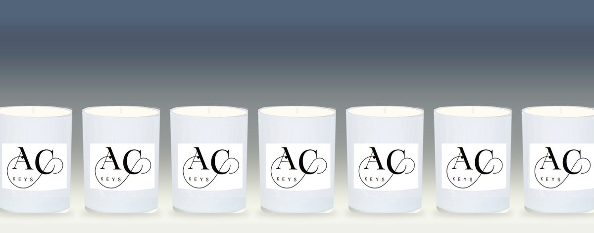 Row of white scented candles, each with a custom company logo label, on a soft grey background