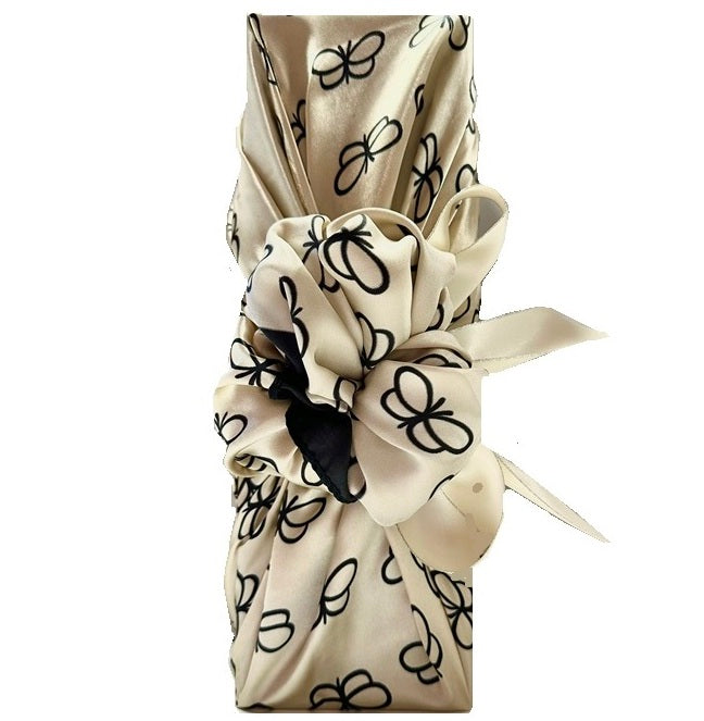 Champagne bottle wrapped Furoshiki-style in an ivory silky scarf with black butterflies, tied in a bow