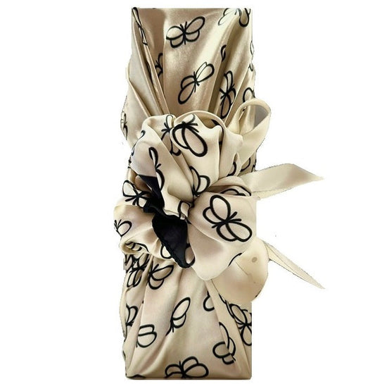 Champagne bottle wrapped Furoshiki-style in an ivory silky scarf with black butterflies, tied in a bow